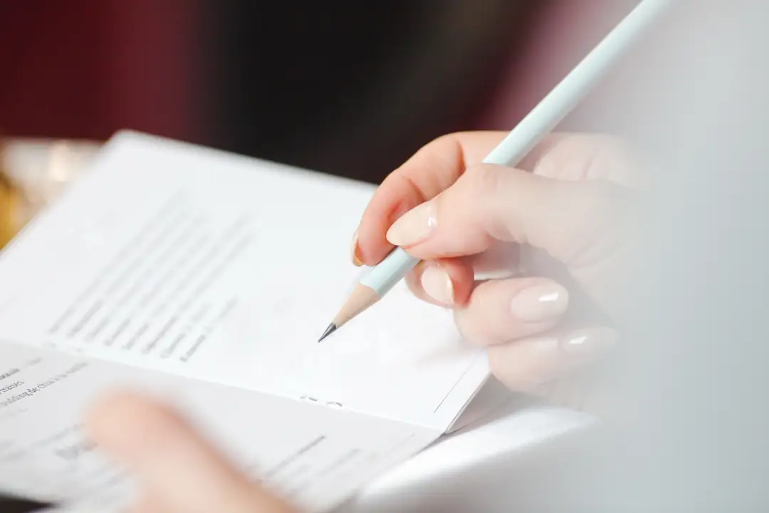 A hand holding a pencil above an open notebook