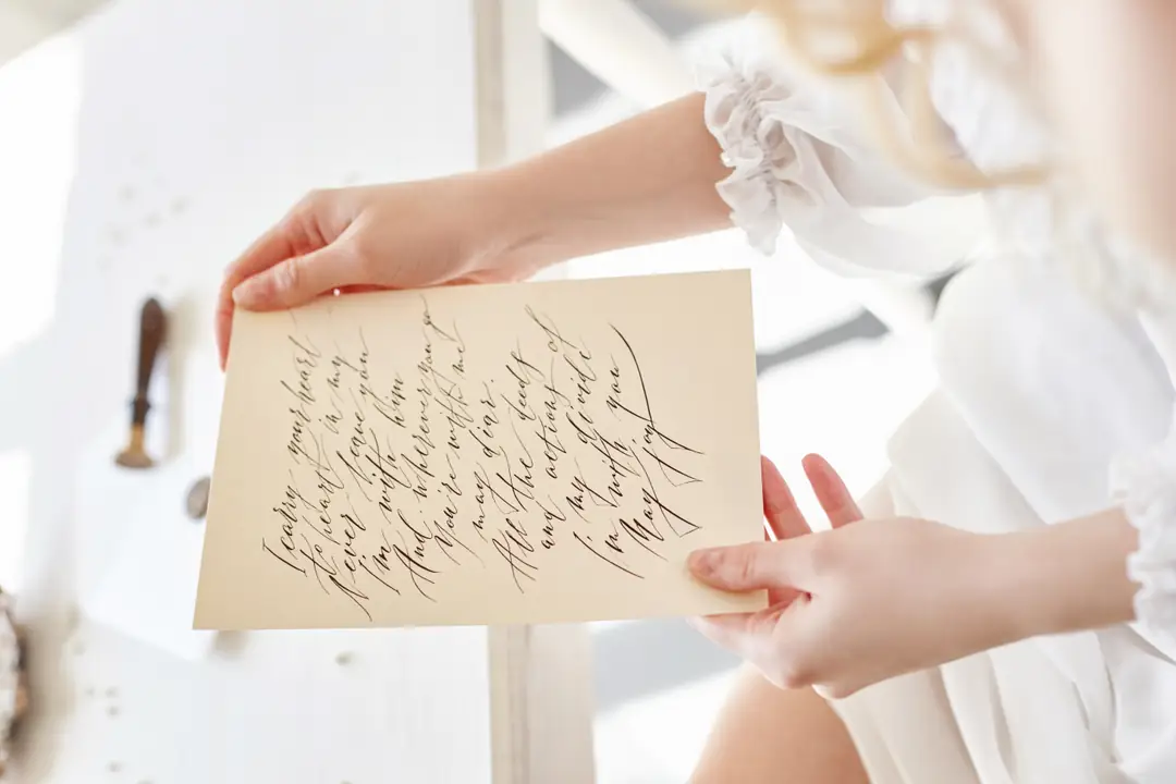 Hands holding a handwritten letter beside a bright window