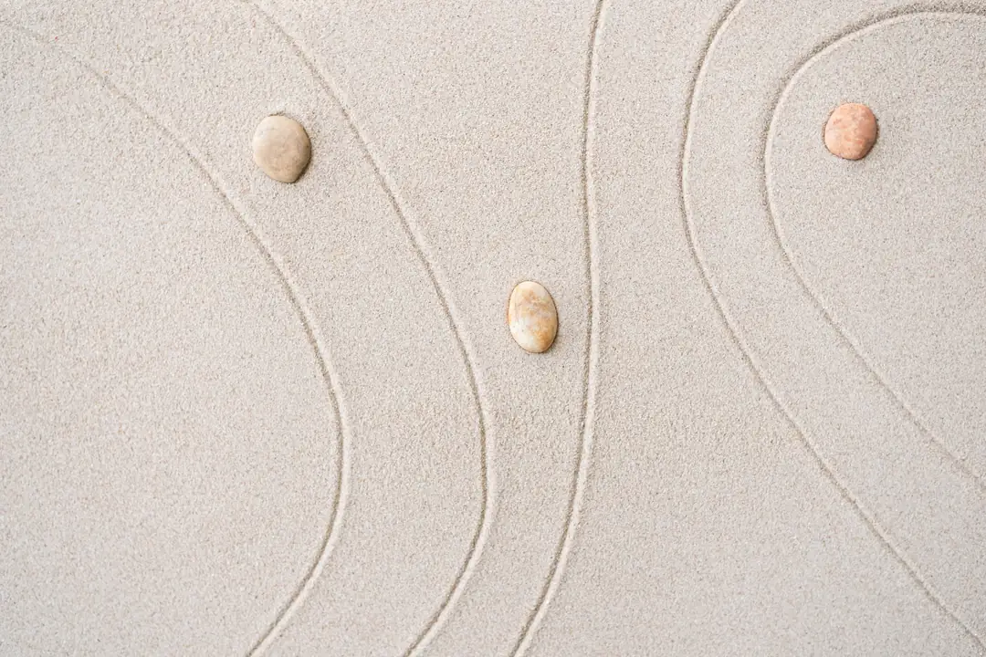 Small smooth stones beside curved lines in pale sand