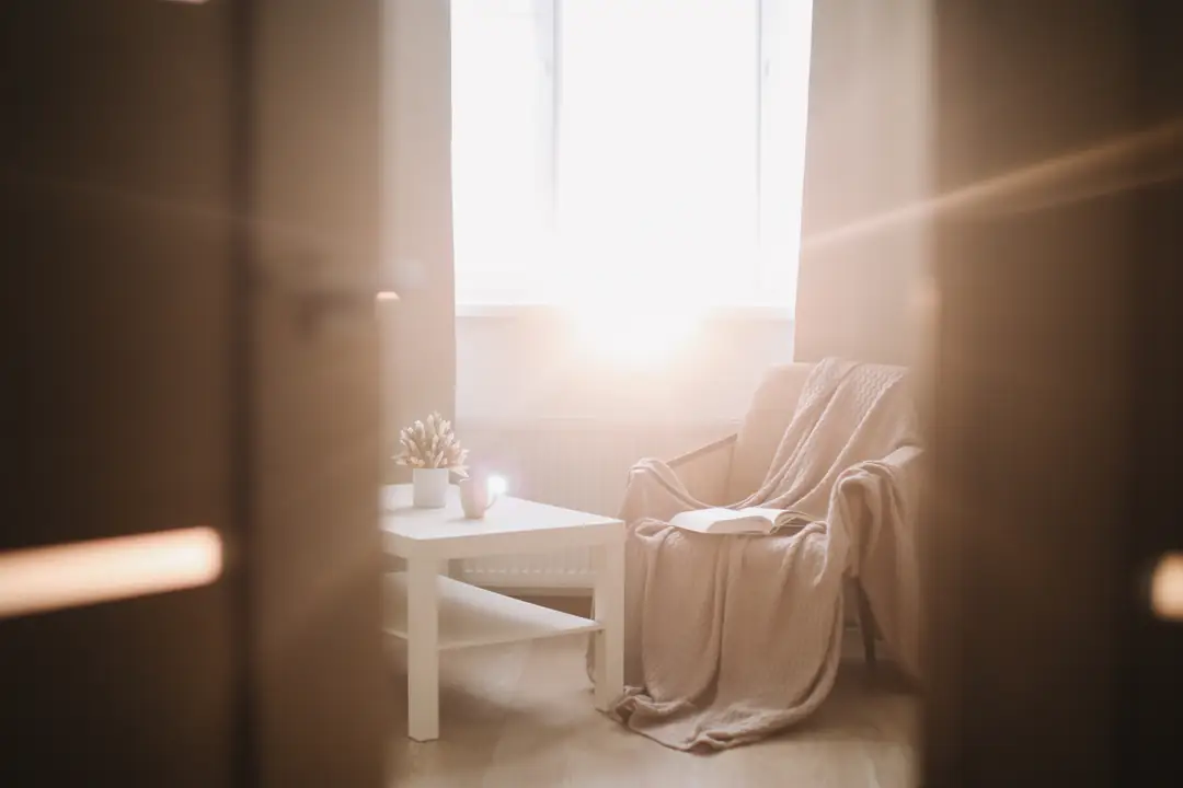 Sunlight falling across a blanket-covered armchair through an open doorway