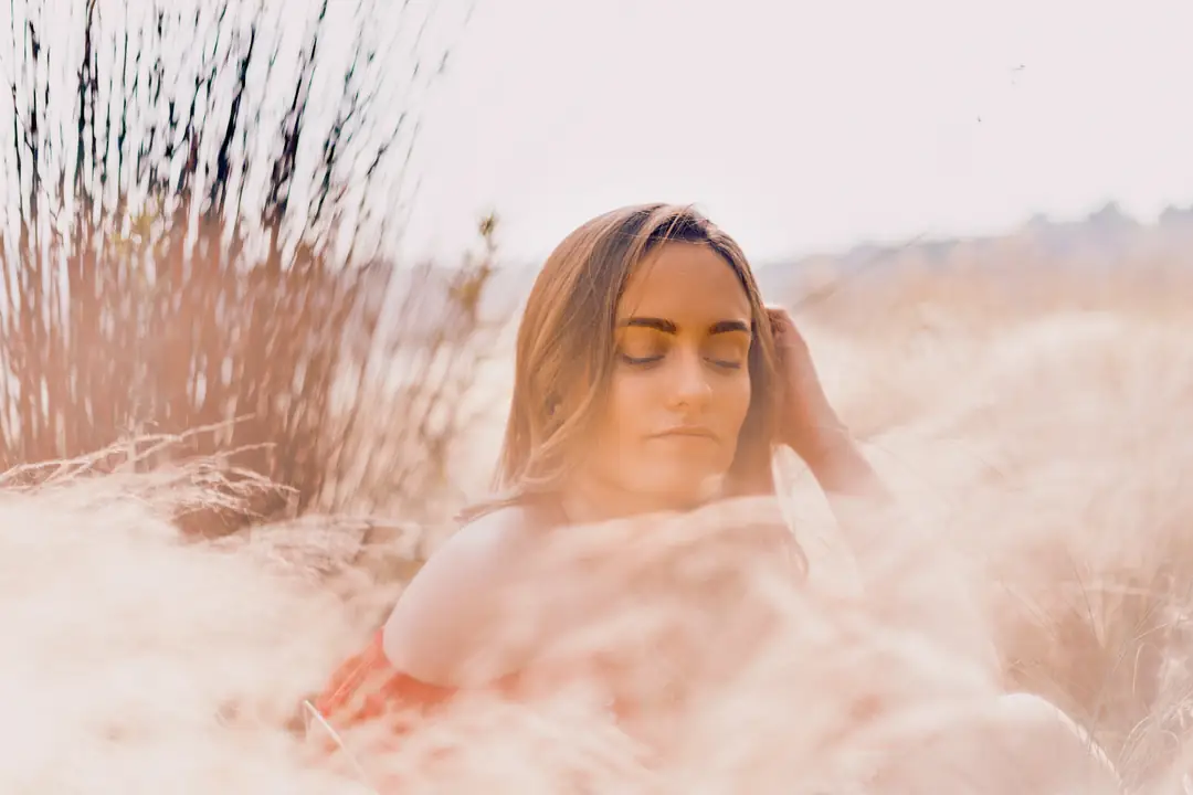 A woman with closed eyes surrounded by softly blurred grasses