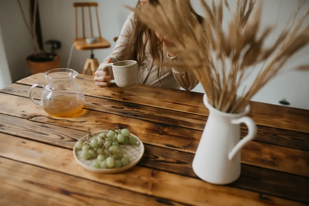 A person holding a mug at a wooden table with a teapot and grapes
