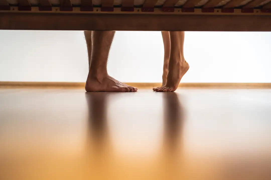 Bare feet resting on a wooden floor beneath a table