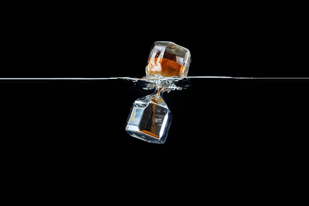 A glass hourglass partly submerged in water against a black background