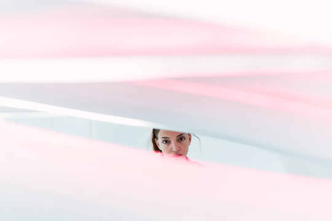 A woman reflected in a narrow mirror between soft pink panels