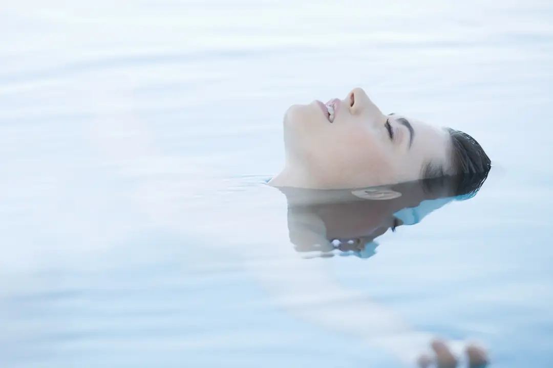 A woman floating face up in still pale blue water