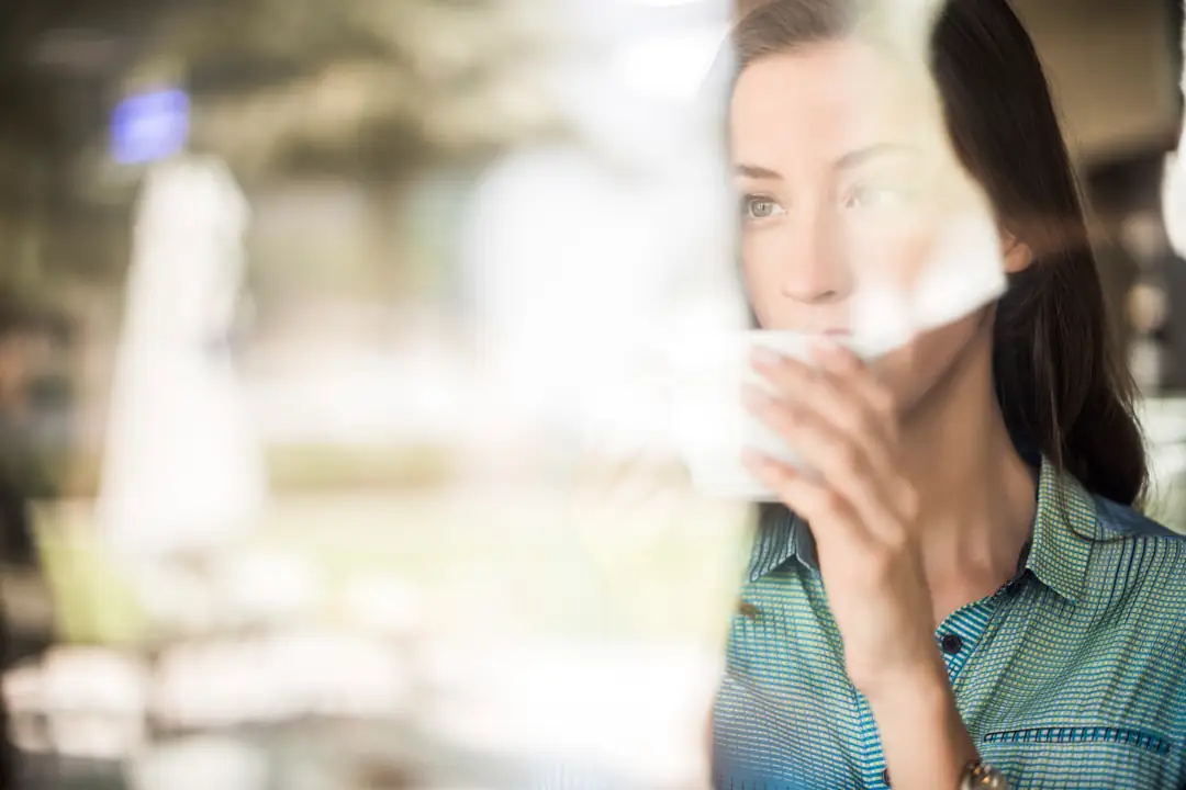 A thoughtful woman holding a cup beside a window